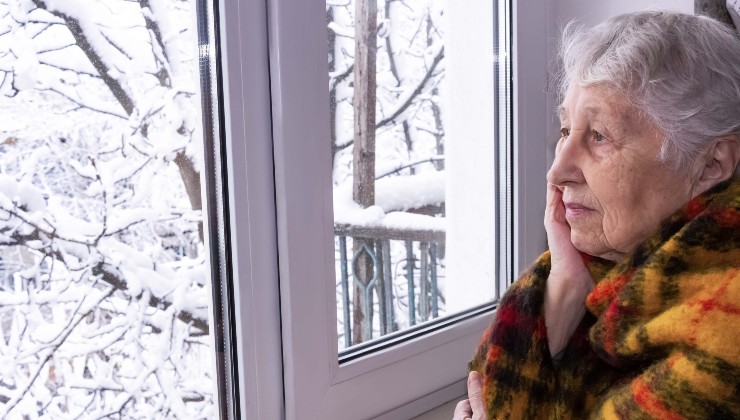 Una signora anziana guarda la neve fuori dalla finestra